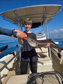 A young angler proudly displaying a large fish aboard a boat in calm waters, showcasing a successful fishing trip.