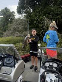 A young angler proudly displaying a large catfish while fishing from a boat in a lush, green environment.