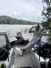 A fisherman relaxing inside a boat on a serene lake, showcasing the boat's interior with a scenic backdrop of lush greenery.
