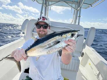 Angler proudly displaying a large Tuna aboard a fishing boat in open waters, showcasing a successful day of deep-sea fishing.