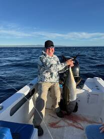 An angler proudly displaying a large Yellowfin Tuna aboard a fishing boat in open waters, showcasing a successful deep-sea fishing trip.
