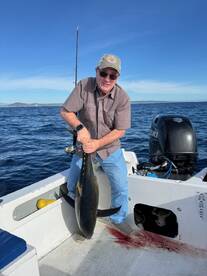 An angler proudly displaying a large Yellowfin Tuna on a fishing boat, showcasing a successful deep-sea fishing trip.