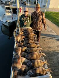 Two anglers proudly displaying a large catch of tilapia arranged on a board at the dock, showcasing a successful fishing trip.