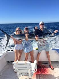 Three anglers proudly displaying a large Marlin on a fishing charter in open waters.