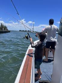 A young angler casting a fishing line from the boat while enjoying a sunny day on the water with family.