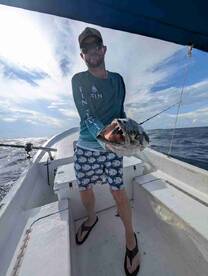 Angler holding a large fish on a small boat during a fishing trip, showcasing the catch against a scenic ocean backdrop.