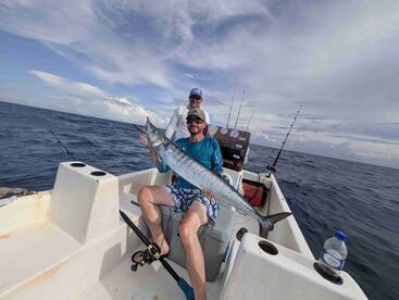 Angler proudly displaying a large Barracuda while fishing from a small boat in open waters.