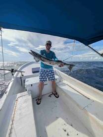 Angler proudly displaying a large Barracuda aboard a fishing boat in open waters.