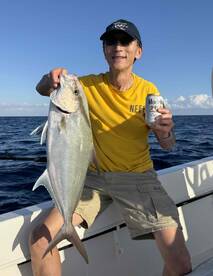 An angler proudly displaying a large fish while enjoying a drink on a fishing trip in open waters.