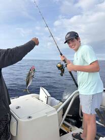 A young angler is reeling in a Mahi Mahi while fishing on a boat, showcasing an exciting moment on the water.