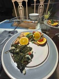 A dinner setting featuring a plate of fish garnished with oranges and a side of greens, showcasing a home-cooked meal.