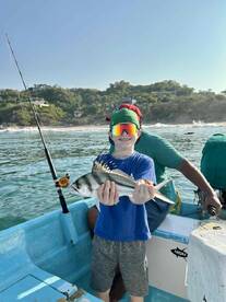 A young angler proudly displaying a caught fish while fishing from a small boat in a coastal setting.
