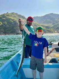 A young angler proudly displaying a fish while fishing with an adult in a scenic coastal setting.