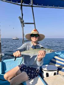 An angler proudly displaying a large Spanish Mackerel while fishing on a small boat in open waters.