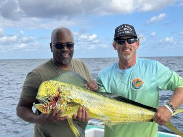 Two anglers proudly displaying a large Mahi Mahi while fishing offshore, showcasing a successful day on the water.