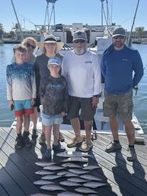 A family poses with their catch of fish on a dock after a successful fishing trip, showcasing a variety of species.