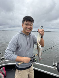 Angler smiling while holding two caught fish, showcasing a successful fishing trip on a cloudy day.