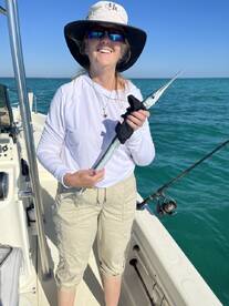 A smiling angler proudly displays a Barracuda while fishing on a boat in clear blue waters.