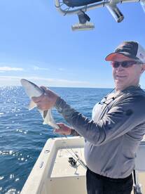 An angler proudly displaying a caught shark while fishing on a sunny day at sea.