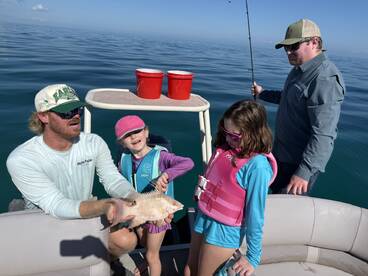 A young angler joyfully displays a caught fish while enjoying a family fishing trip on a calm day at sea.