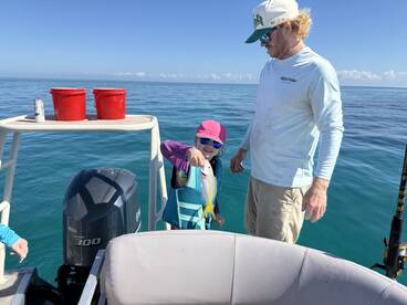 A young angler in a life jacket proudly shows off a fish while fishing on a boat in clear blue waters.