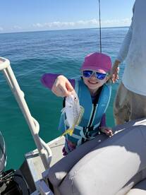 A young angler proudly displaying a small fish while fishing on a boat in clear blue waters.