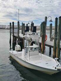 A sleek fishing boat docked at a marina, showcasing its clean lines and fishing amenities against a scenic backdrop.