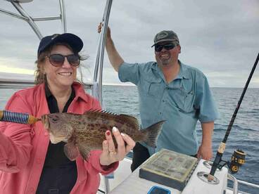 A happy angler proudly displaying a large grouper while fishing on a boat, enjoying a day out on the water.