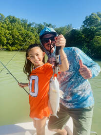 A young angler and an adult proudly displaying a freshly caught fish while enjoying a day of fishing in a scenic mangrove setting.