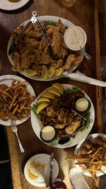 A variety of fried seafood dishes served on plates, including fried fish, fries, and dipping sauces, likely from a seafood restaurant.