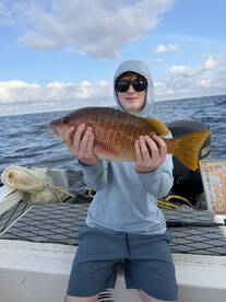 A young angler proudly displaying a colorful Snapper while fishing on a boat, showcasing a beautiful day on the water.