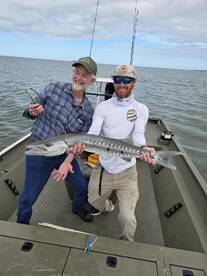 Two anglers proudly displaying a large Barracuda on a fishing boat, showcasing a successful day on the water.