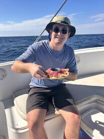 A young man enjoying a meal on a boat, with a scenic ocean backdrop.