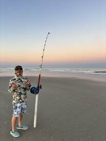 A young angler poses with a fishing rod on the beach during a serene sunset, showcasing the excitement of surf fishing.