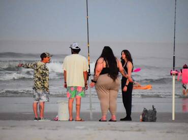 Group of friends gathered on the beach, engaged in conversation while fishing rods are set up nearby.