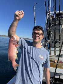 A young angler proudly displaying a colorful Snapper while fishing on a sunny day.