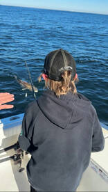 A young angler is engaged in fishing on a boat, with a fish visible in the water, showcasing an exciting moment on the open sea.