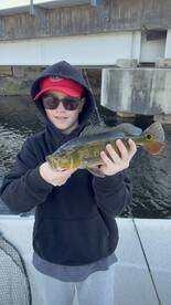 Young angler proudly holding a large Largemouth Bass while fishing under a bridge.