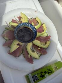 A beautifully arranged plate of sashimi featuring fresh fish, avocado, and cucumber, served with soy sauce, showcasing the culinary delights of a successful fishing trip.