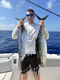 Angler proudly displaying two large Tuna caught during a deep-sea fishing trip.