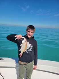 Young angler proudly holding a colorful Snapper while fishing in clear blue waters.
