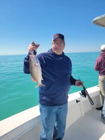 An angler proudly displaying a Snapper caught during a fishing trip on a calm day at sea.