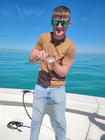A young angler proudly displaying a small fish while fishing on a sunny day in clear blue waters.