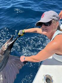 An angler actively reeling in a Sailfish while fishing in deep blue waters, showcasing the excitement of sport fishing.