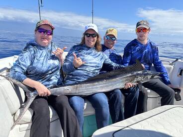 A group of anglers proudly displaying a large Wahoo while fishing in open waters, showcasing their successful catch during a fun day on the boat.