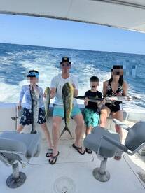 A family proudly displaying their catch of Mahi Mahi and Barracuda while enjoying a day of fishing on a boat.