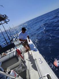 An angler actively reeling in a fish while fishing on a boat in open waters, showcasing the excitement of deep-sea fishing.