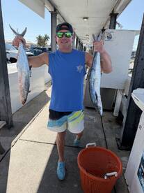 Angler proudly displaying two large fish, likely King Mackerel, while walking along the dock after a successful fishing trip.