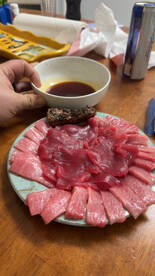A beautifully arranged plate of fresh sashimi, showcasing thinly sliced tuna, accompanied by a dipping sauce, perfect for a seafood feast.