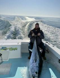 Angler proudly displaying a large Bluefin Tuna on a boat, showcasing a successful offshore fishing trip.